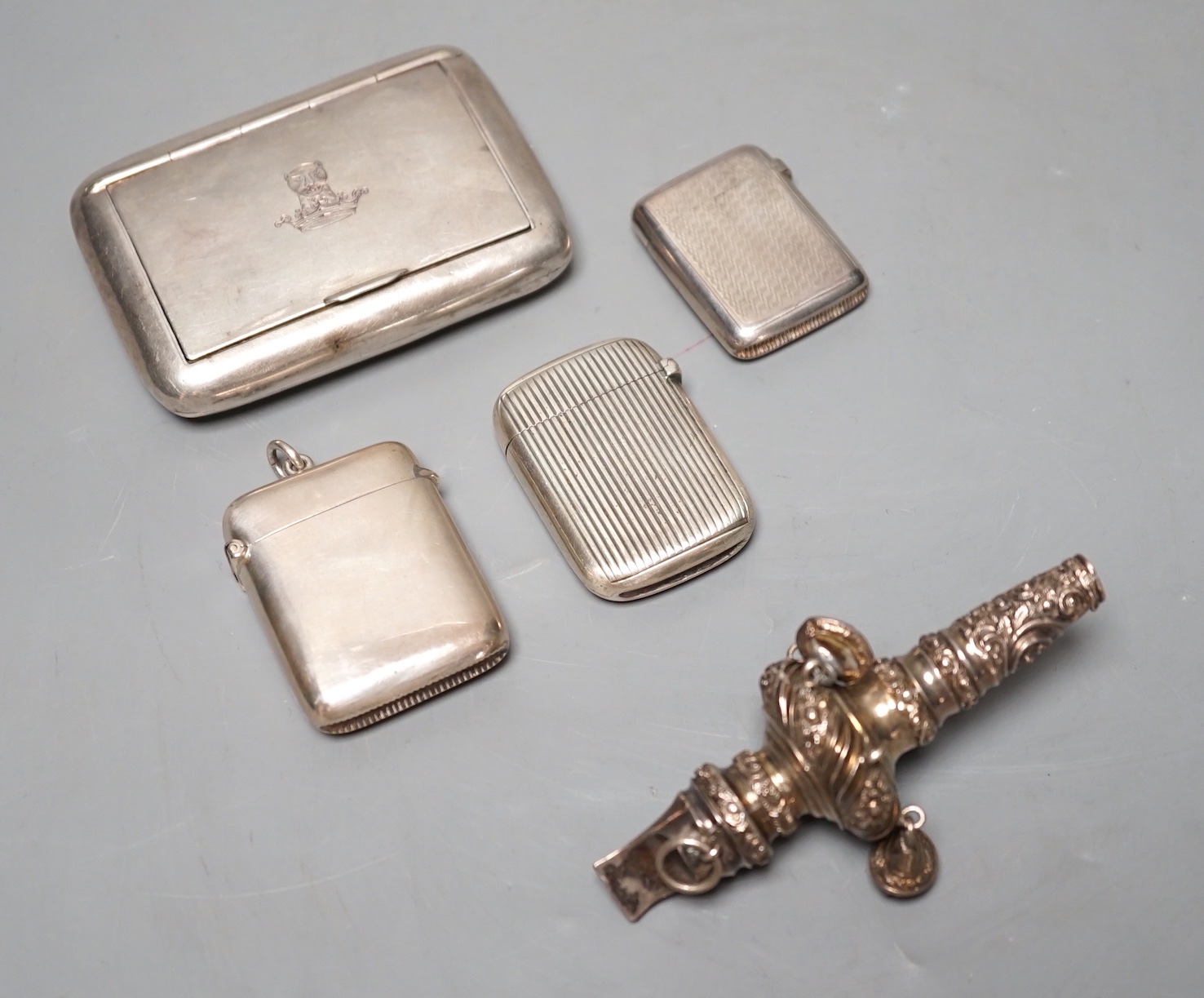 An Edwardian silver snuff box, with engraved crest, Birmingham, 1907, 82mm, three silver vesta cases and an incomplete white metal child's rattle.